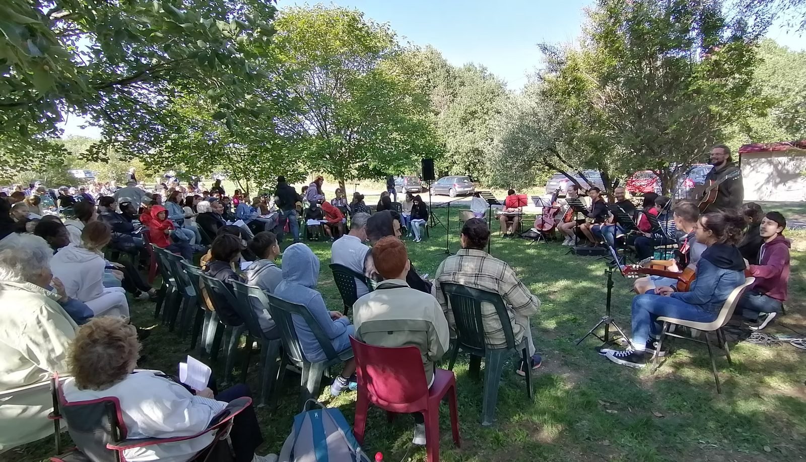 Culte en plein air : l’assemblée réunie sous les arbres, avec les musiciens